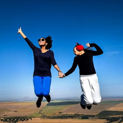 Person joyfully jumping in an open field against the sky.